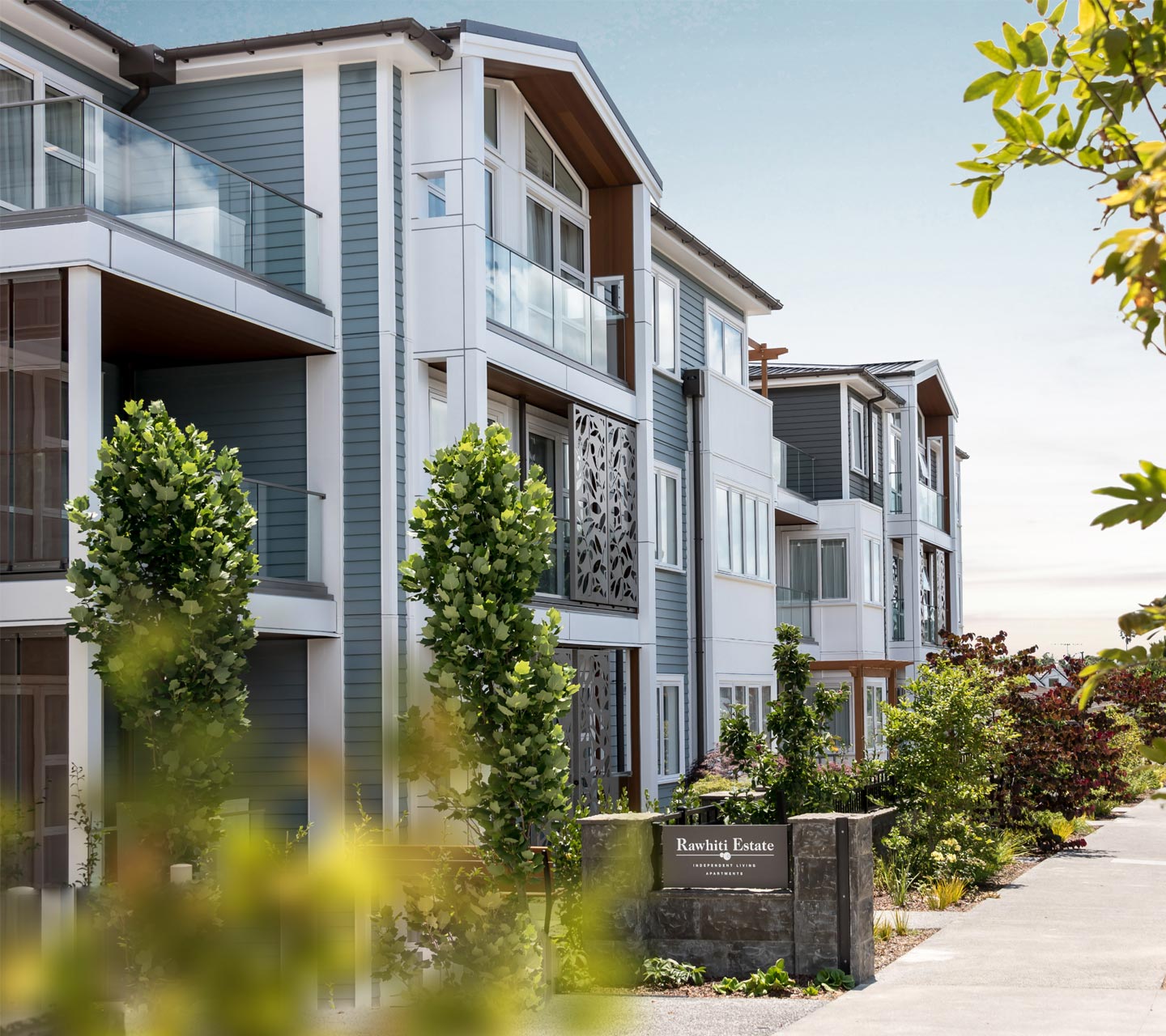 Exterior view of modern apartments at Rawhiti Estate retirement village with glass balconies and landscaped greenery.